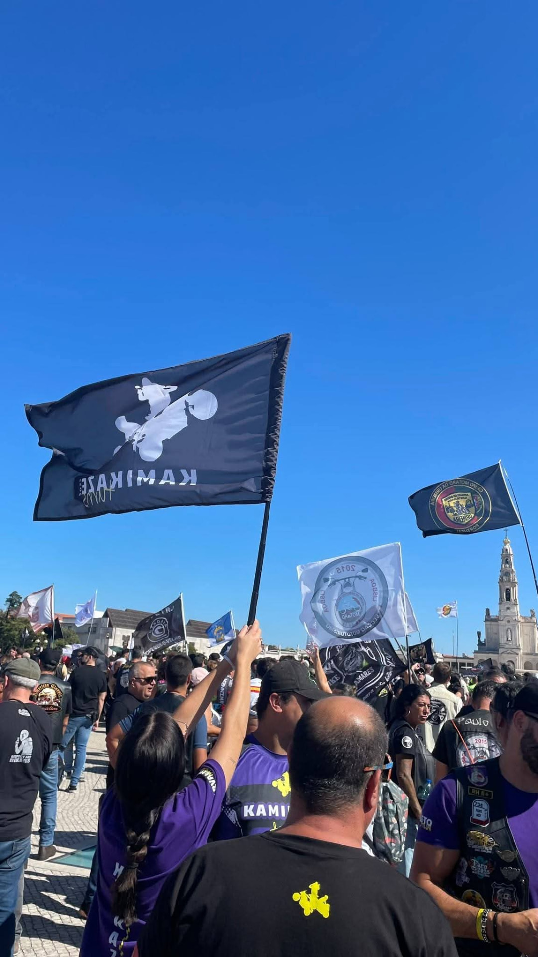 Multidão de motociclistas a agitar bandeiras de clubes ao vento, incluindo a bandeira Kamikaze Turns