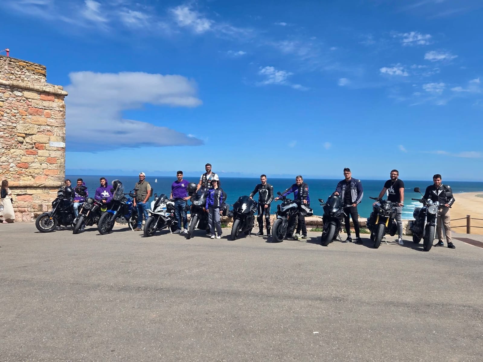Grupo do clube com as motas num miradouro sobre o mar, junto a uma fortaleza de pedra